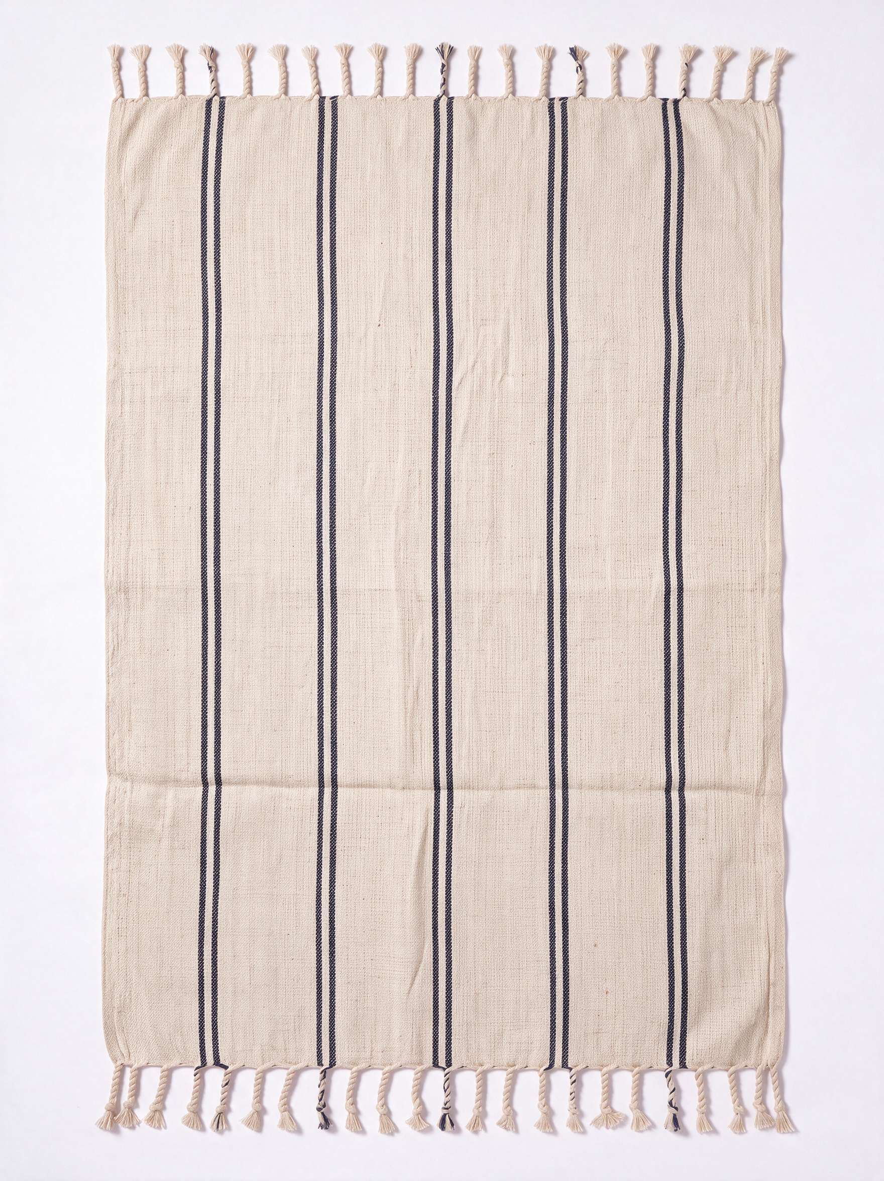 A rectangular beige woven towel with vertical dark gray stripes and fringed tassels on the top and bottom edges, photographed flat against a white background.