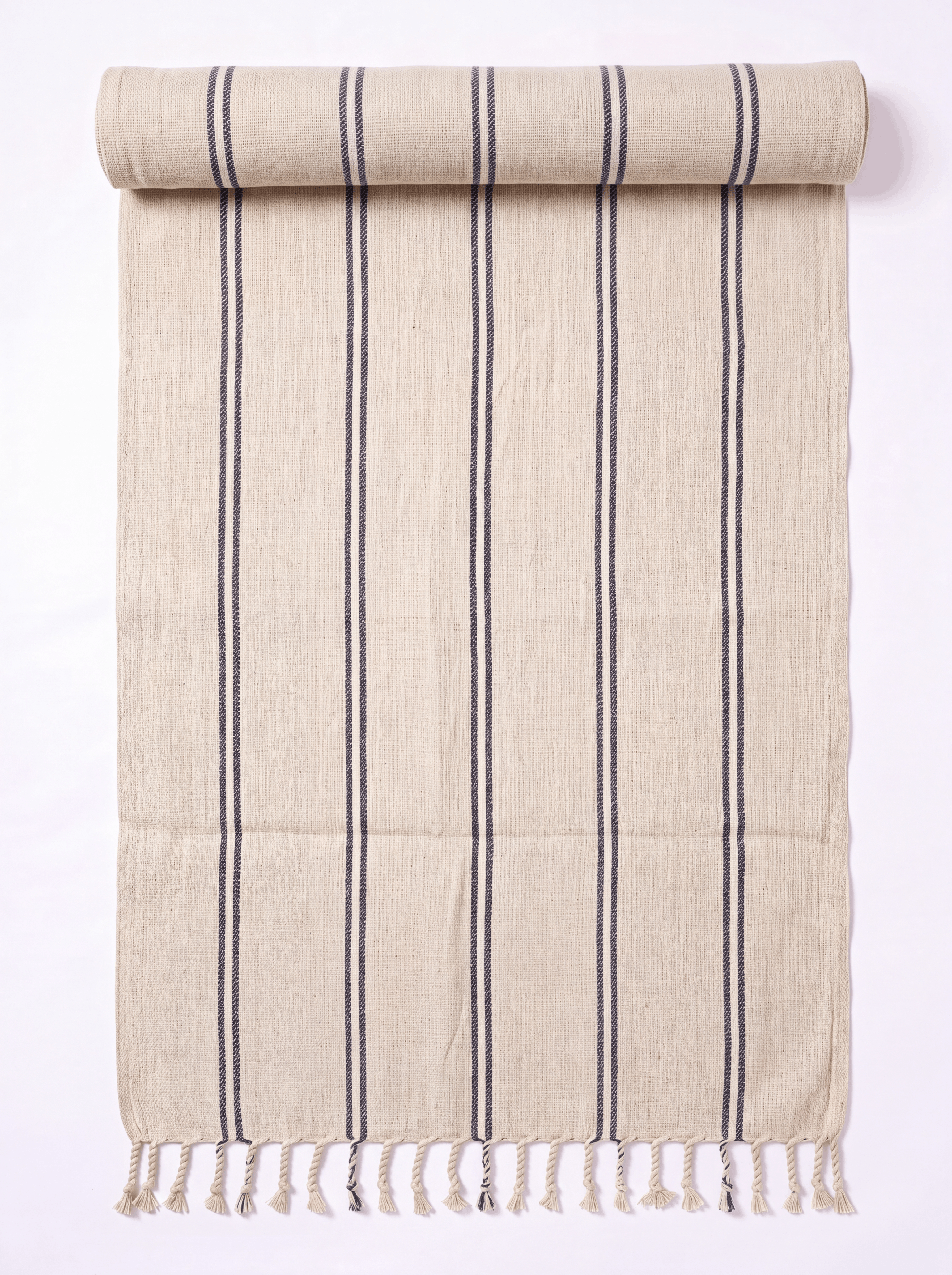 A beige woven towel with vertical dark gray stripes and fringed tassels along one edge, shown partially rolled on a plain white background.
