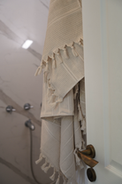 Beige textured towel with tassels hanging on a door handle in a bathroom.
