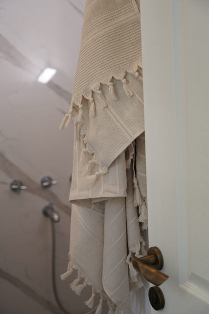 Beige textured towel with tassels hanging on a door handle in a bathroom.