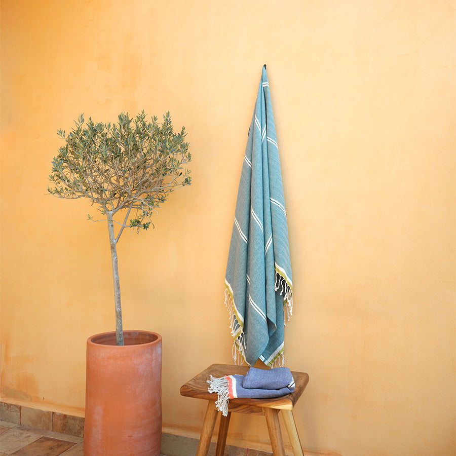 Blue towel with white stripes hanging on a wooden stool against a yellow wall with a potted plant.