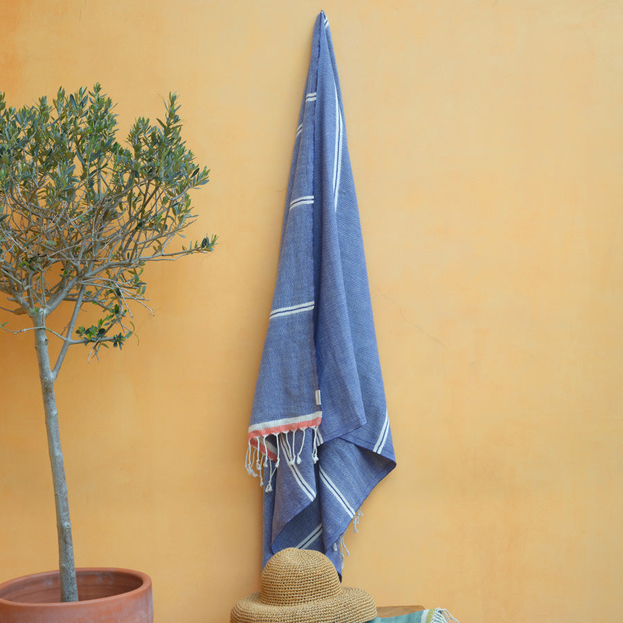 Blue towel hanging on a yellow wall next to a potted plant and straw hat.