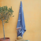 Blue towel hanging on a yellow wall next to a potted plant and straw hat.