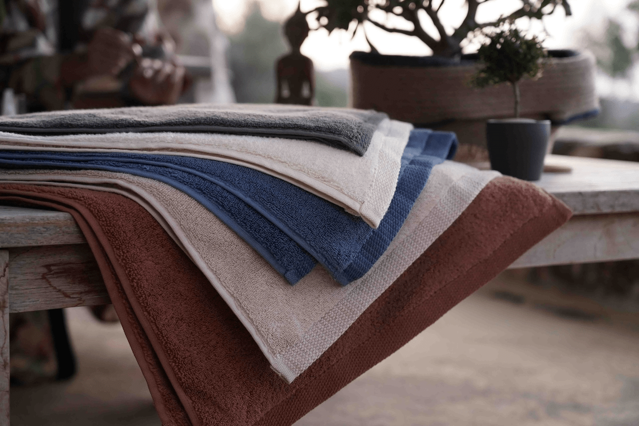 Plush Lite 500-Gram Aegean Cotton Large Organic Bath Towels in Moonlight Pearl, Honey Latte, Charcoal Embrace, Blue Velvet, Cinnamon Charm, and Pure n Raw, fully laid out to showcase their soft texture and range of elegant colours