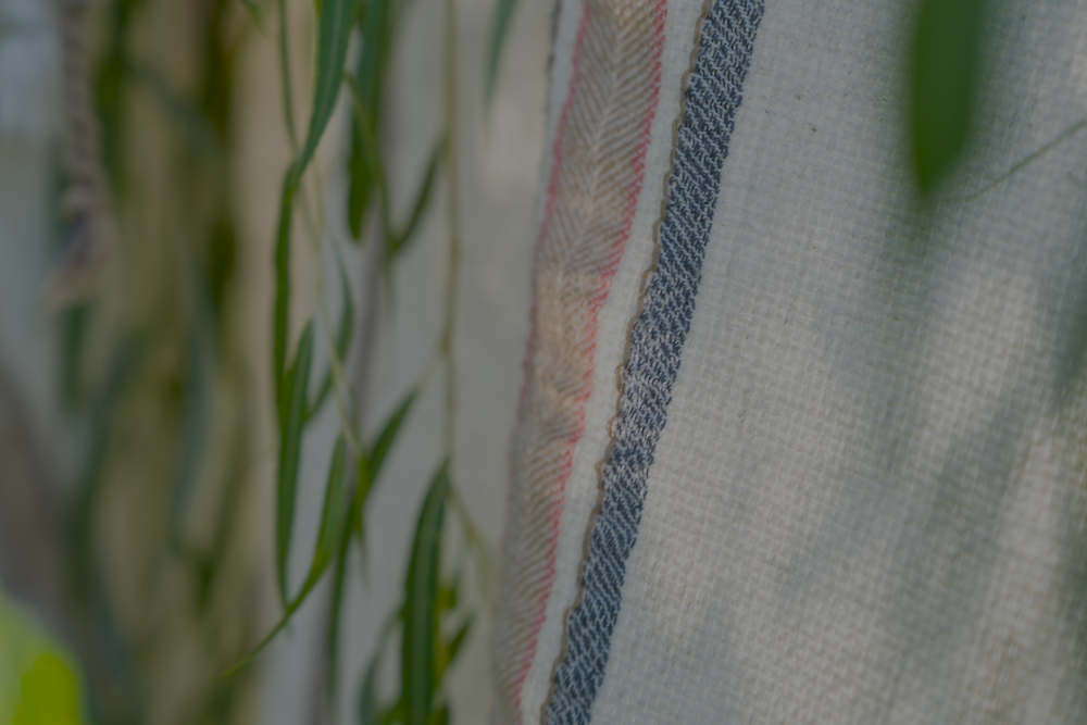 A close-up shot of the luxury organic Elba Turkish towel hanging on a cloth hanger outside, surrounded by green leaves for a natural vibe
