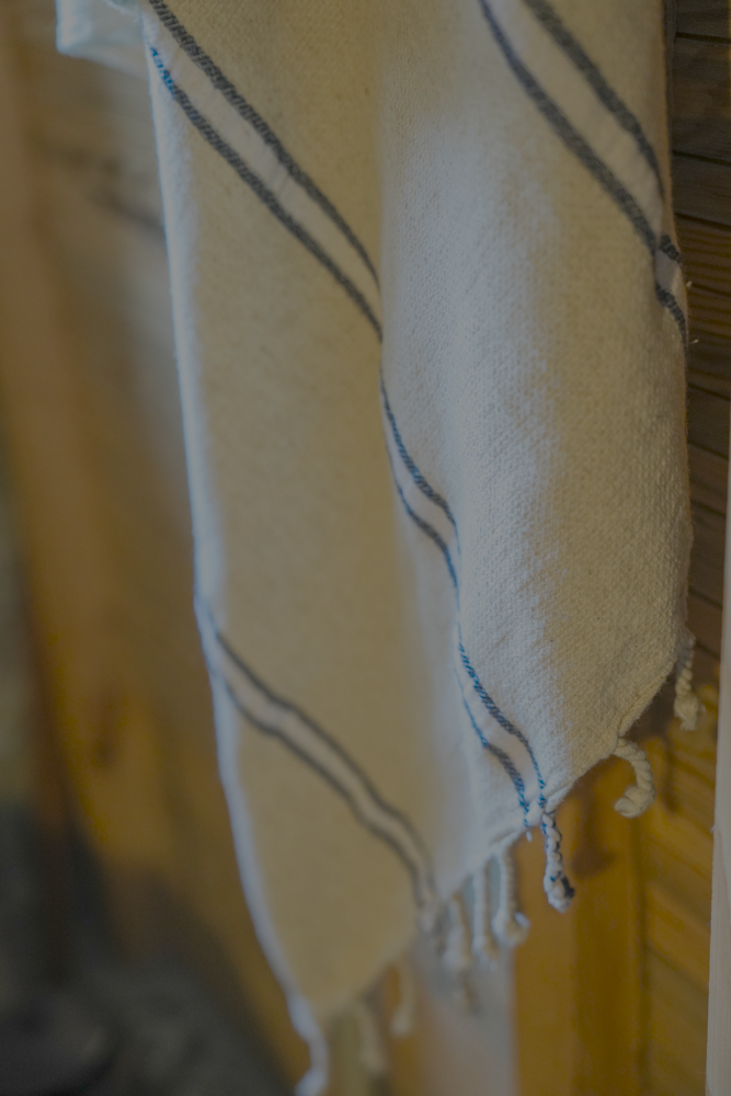 Blue and white eco friendly Anakao 215 gram Aegean Cotton and Linen Turkish towel hanging on wooden wall highlighting organic bath towel quality