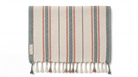 A striped Turkish towel with cream, slate blue, and terracotta stripes, finished with a fringed tassel edge. A small white label on the left edge reads 'Turkish Cotton'.