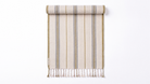 A vertical striped towel with fringe at the bottom, shown hanging flat against a plain white background. The color palette features a warm cream base with vertical stripes in muted blue-gray, olive green, and tan.