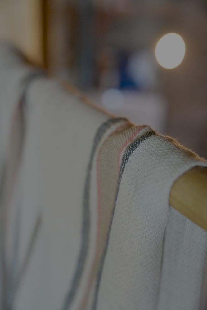 Luxury and organic Sand & Navy Elba Turkish Towel hanging on a cloth hanger in a room
