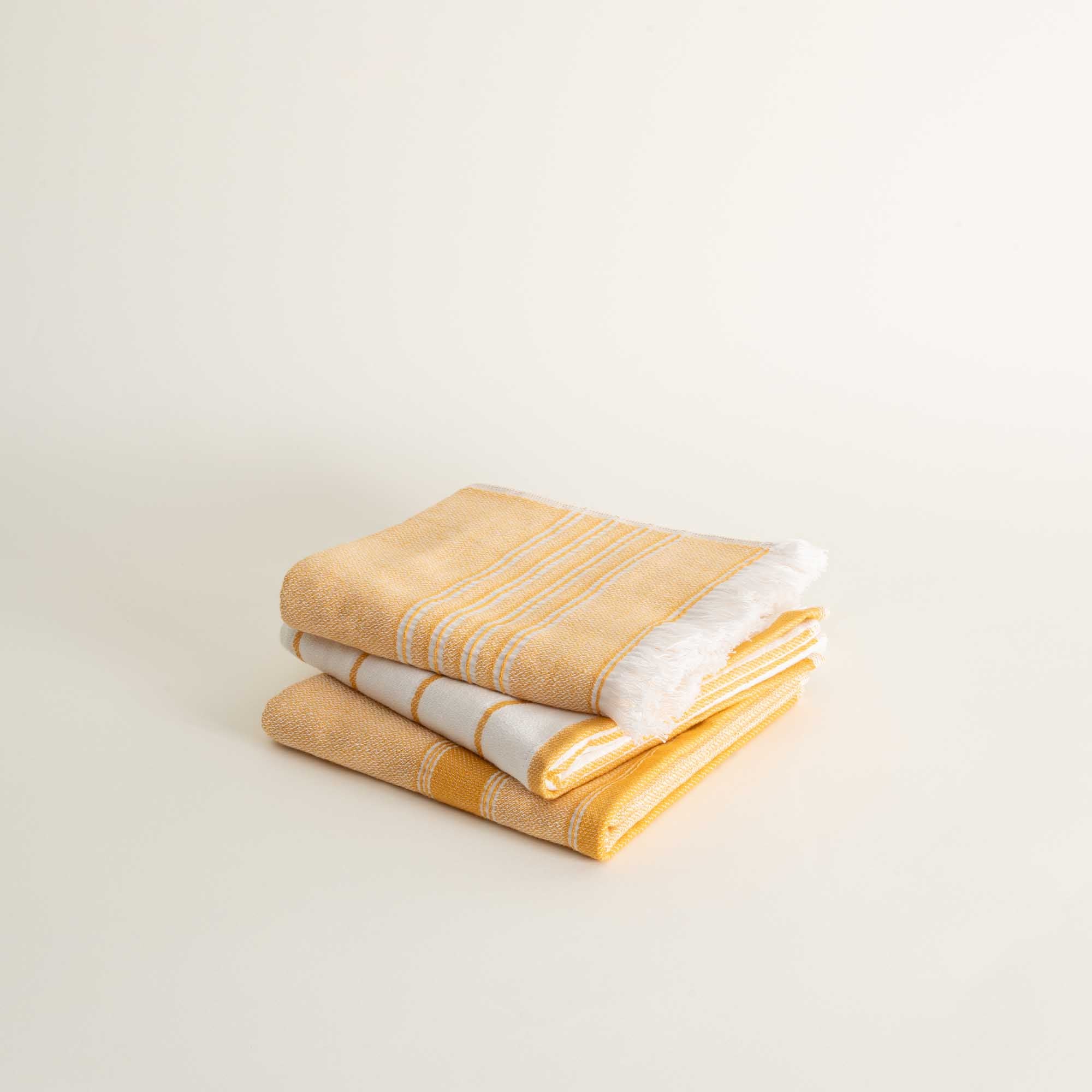 Stack of yellow and white striped towels on a light beige background