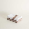 Two folded towels, one white with a brown stripe and one brown, on a light beige background.
