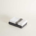 Two folded towels, one white with a gray stripe and one gray, on a light beige background.