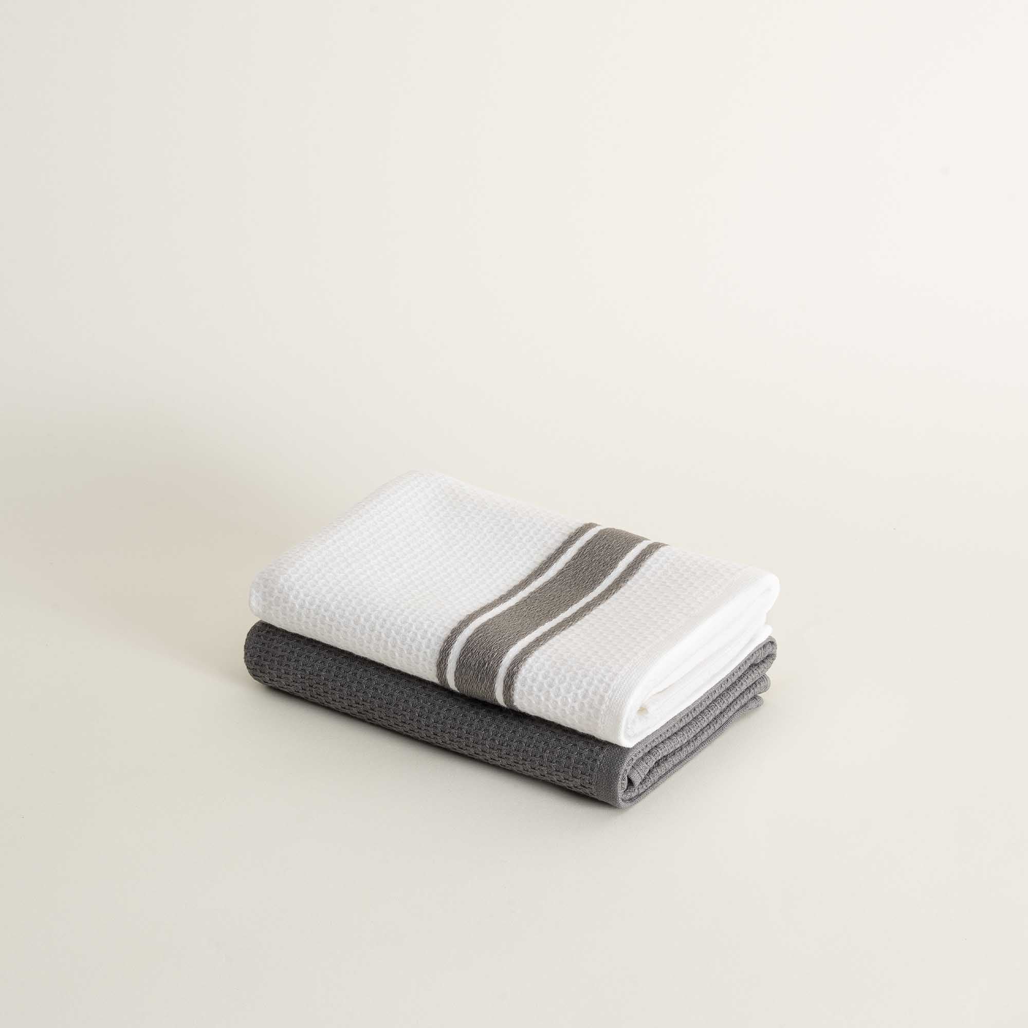 Two folded towels, one white with a gray stripe and one gray, on a light beige background.