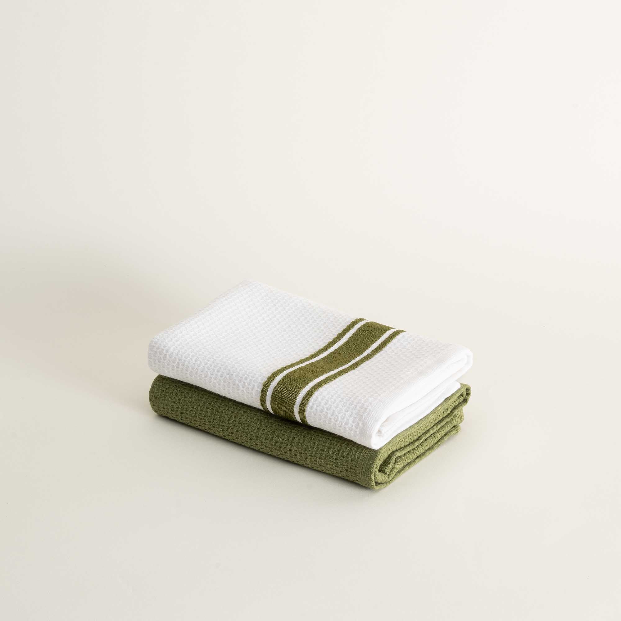 Two folded towels, one white with a green stripe and the other green, on a light beige background.