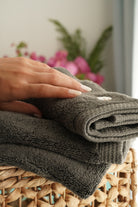 Minoa USA Canada Jasper organic Aegean cotton luxury bath towel set with a woman's hand touching it, highlighting soft plush texture, elegant design, and sustainable luxury