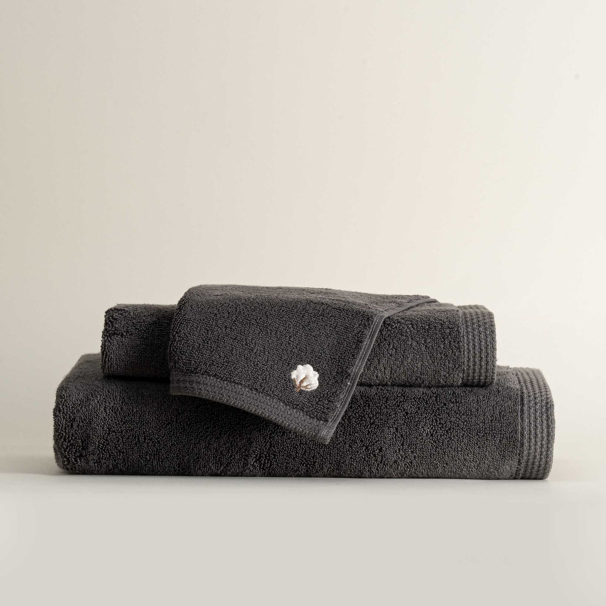 Three folded Jasper 600-gram organic Aegean cotton luxury bath, hand, and washcloth towels in Charcoal Charm, showcasing soft plush texture, deep color, and luxurious fabric
