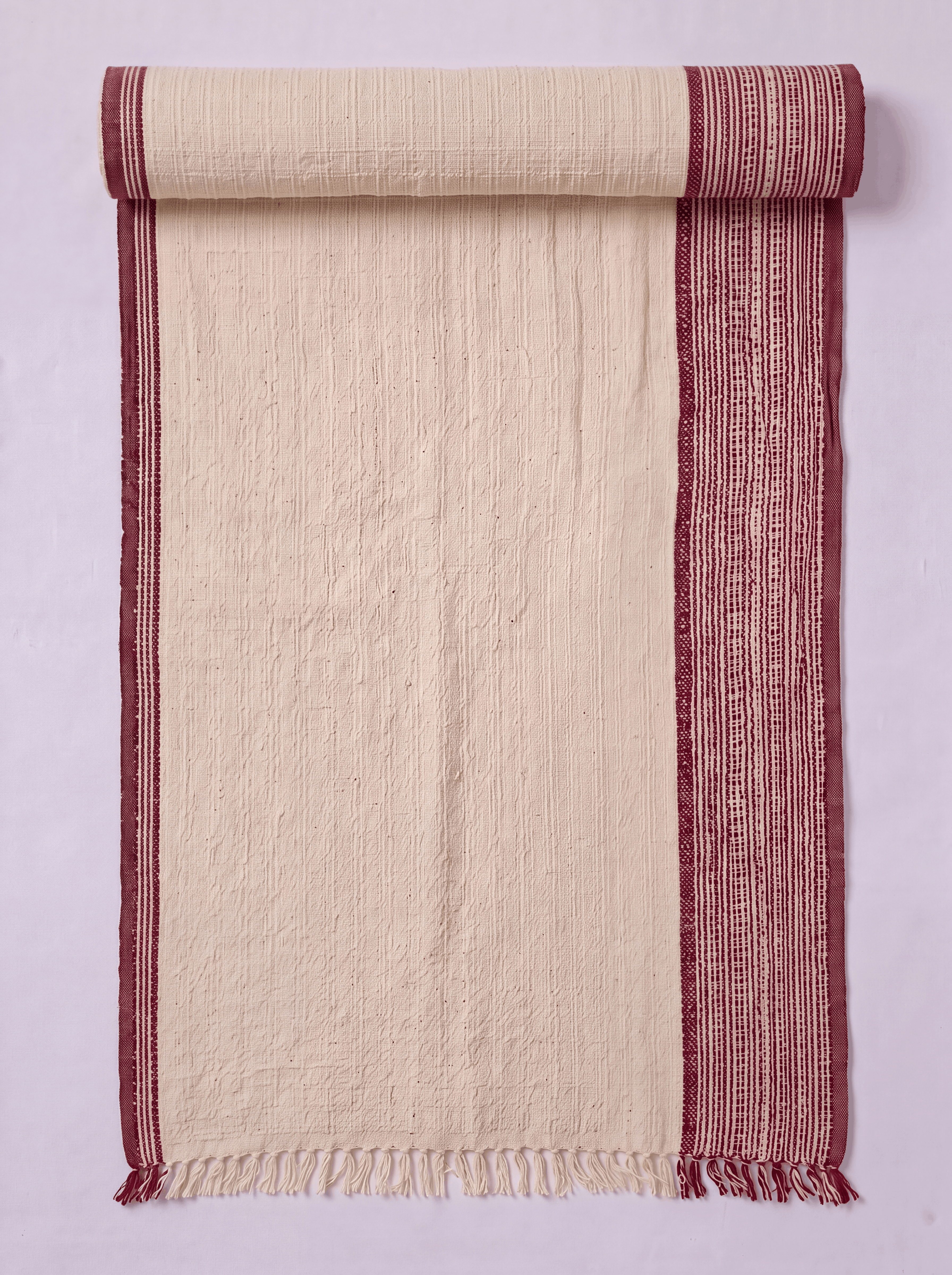 A cream-colored towel with rust-red borders, shown partially unrolled against a light lavender background.