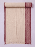 A cream-colored towel with rust-red borders, shown partially unrolled against a light lavender background.