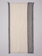 A rectangular woven towel featuring a wide off-white center panel, thin dark navy borders on the left, and a wider dark blue vertical patterned band on the right, finished with short fringe on both ends.