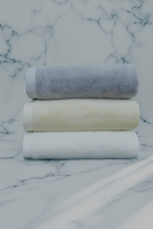 Three Monte Rosa towels stacked on top of each other. One white, one beige, and one grey.