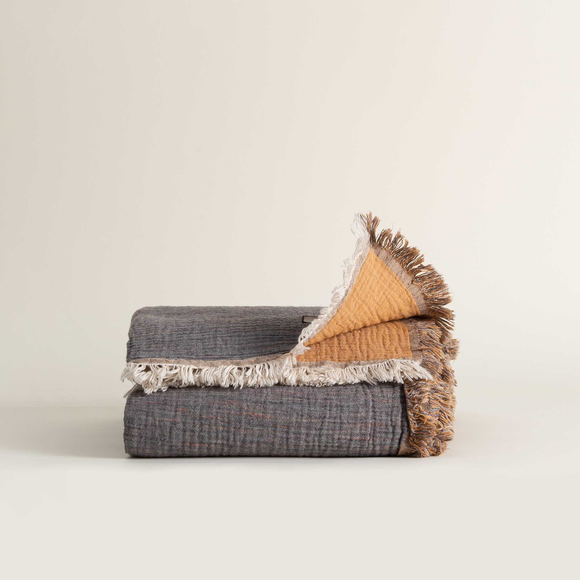 Folded reversible Muna organic gauze bed spread in Mustard, vibrant color, soft texture, neat folds with organic cotton sheets.