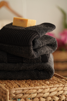Stack of dark towels with a bar of soap on top, placed on a woven surface.