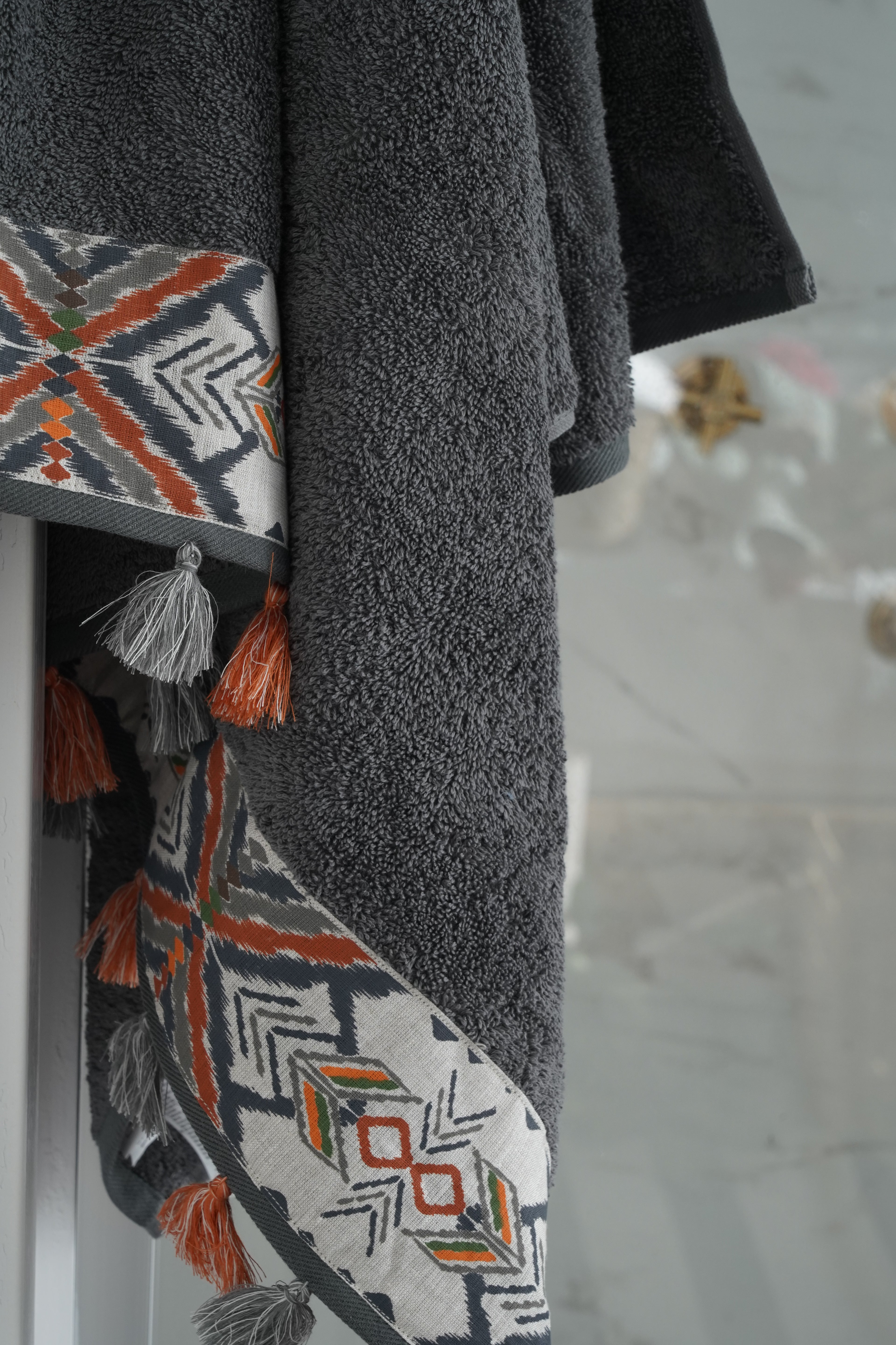 Gray towel with a patterned border featuring geometric designs and tassels on a light gray background.