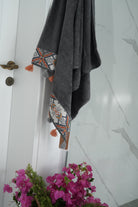 Gray towel with geometric pattern hanging on a door, with pink flowers in the foreground.