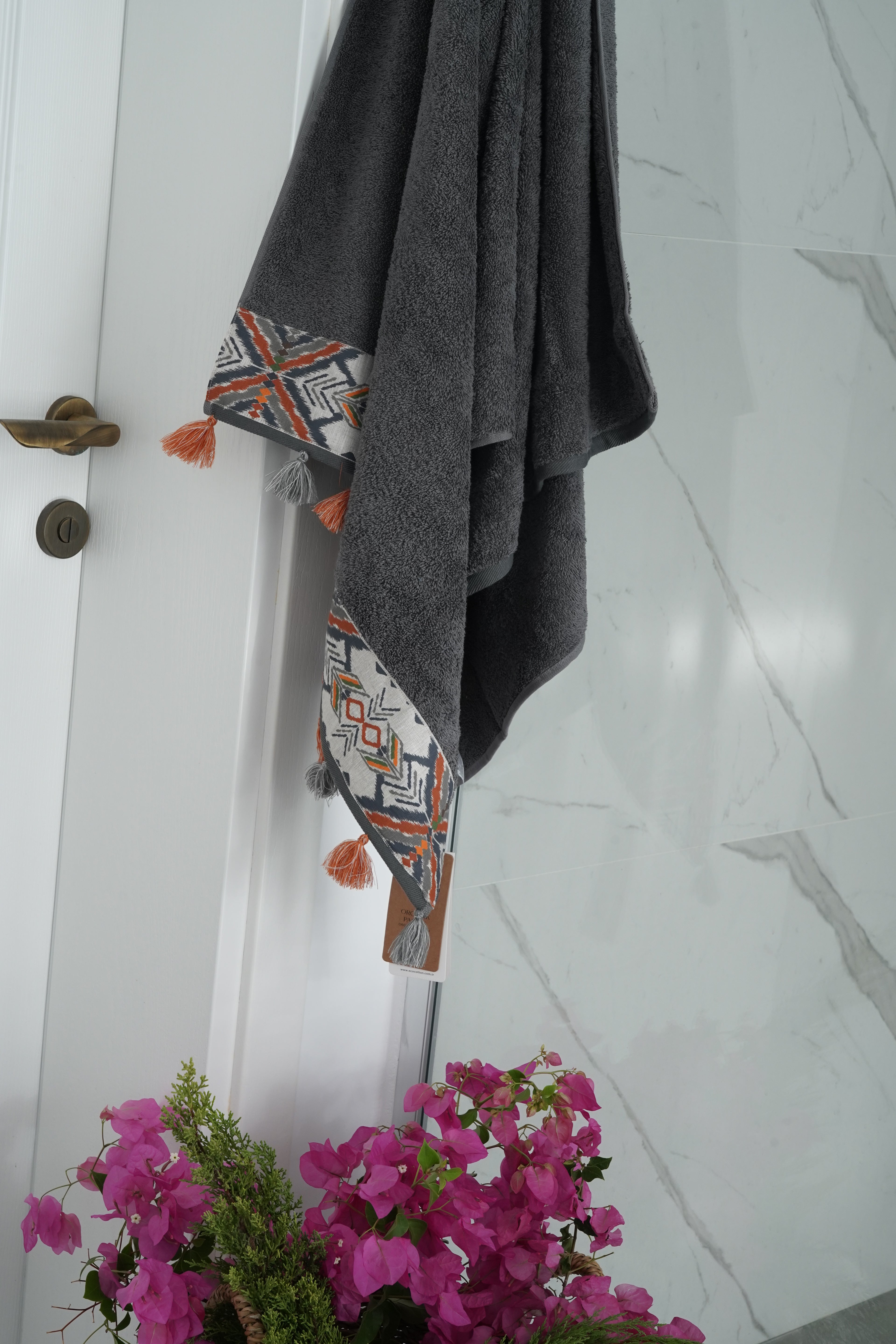 Gray towel with geometric pattern hanging on a door, with pink flowers in the foreground.