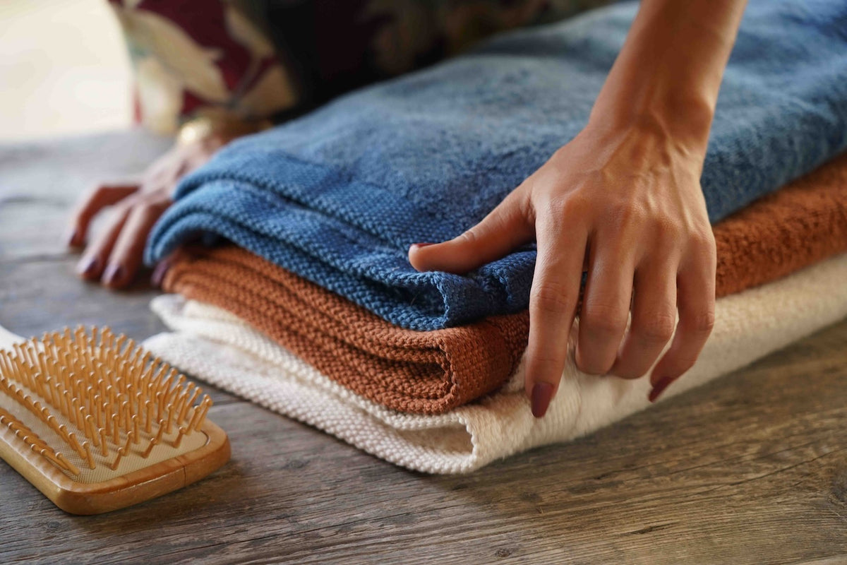 Person folding towels on a wooden surface with a wooden brush nearby