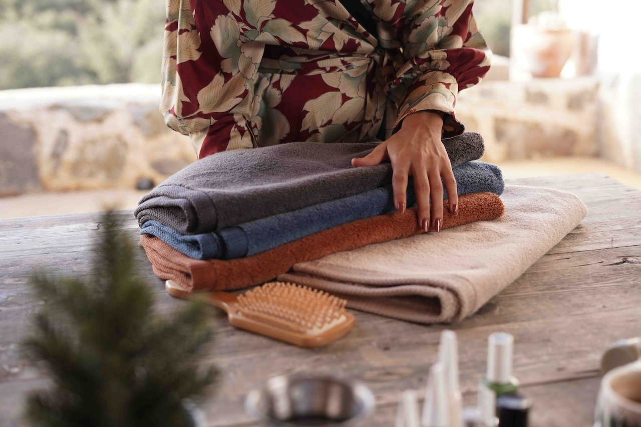 Person folding towels on a wooden surface with a blurred natural background