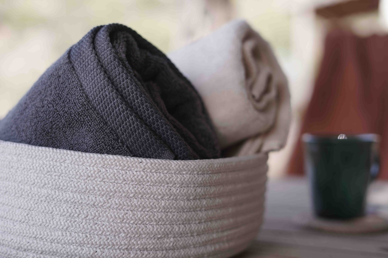 Folded dark gray and beige towels in a woven basket with a blurred background