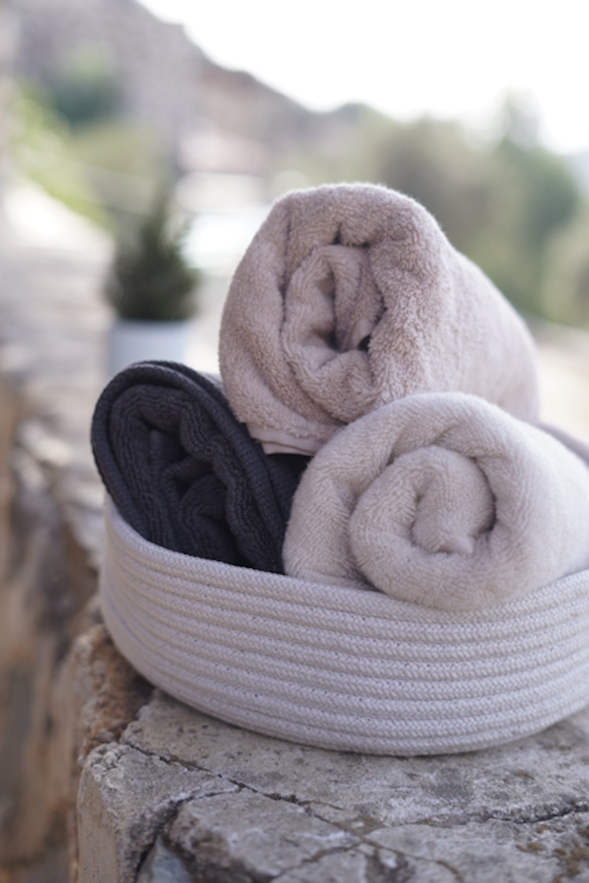 Three folded towels in a woven basket on stone steps with a blurred natural background