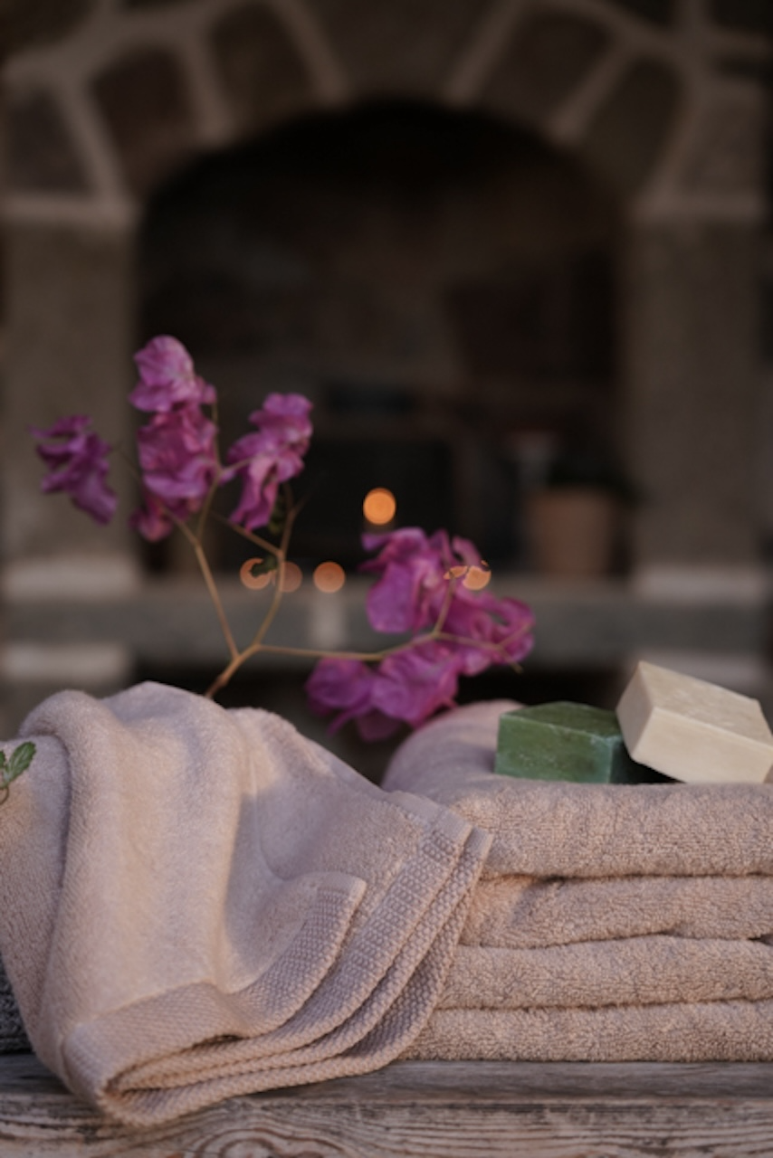 Folded towels with a bar of soap and purple flowers on a wooden surface with a blurred background.