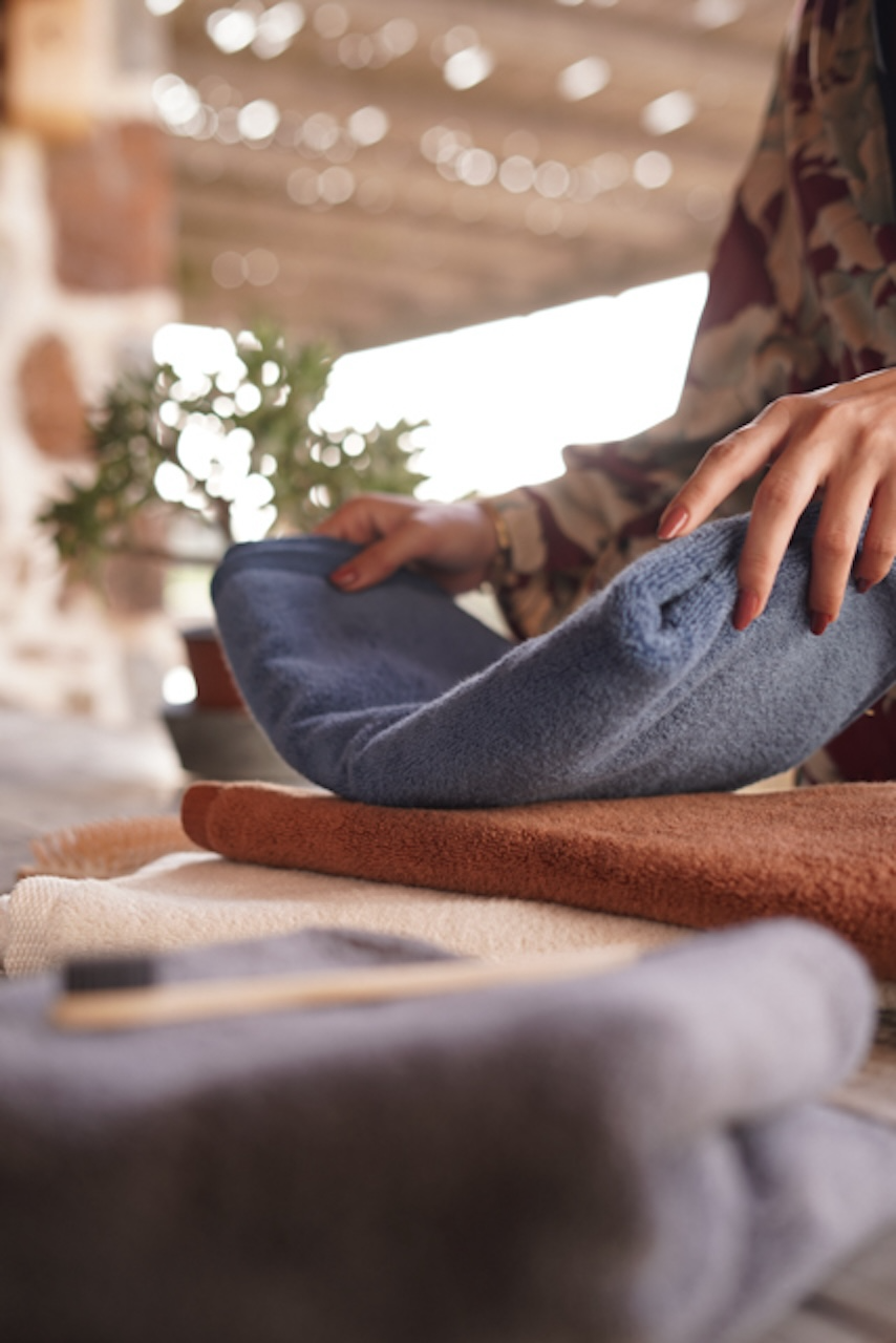 A person laying a blue towel on top of an orange towel on a table.