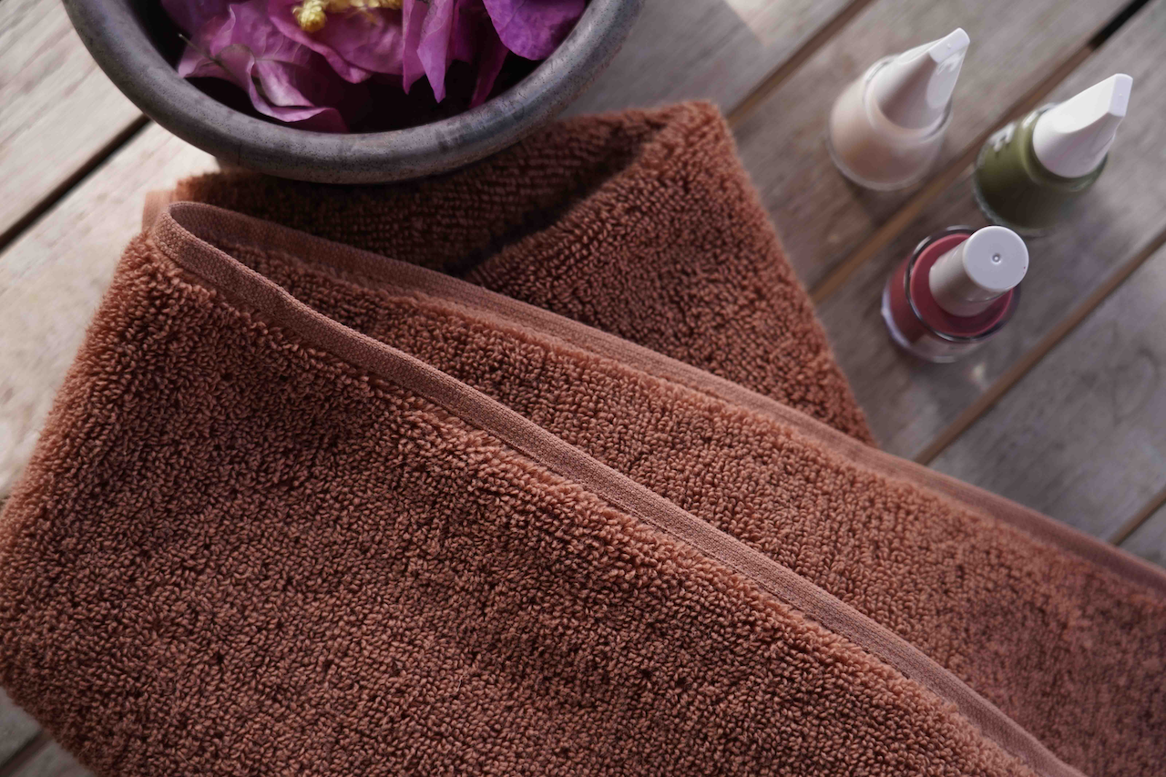 Brown towel on a wooden surface with bottles and a bowl in the background