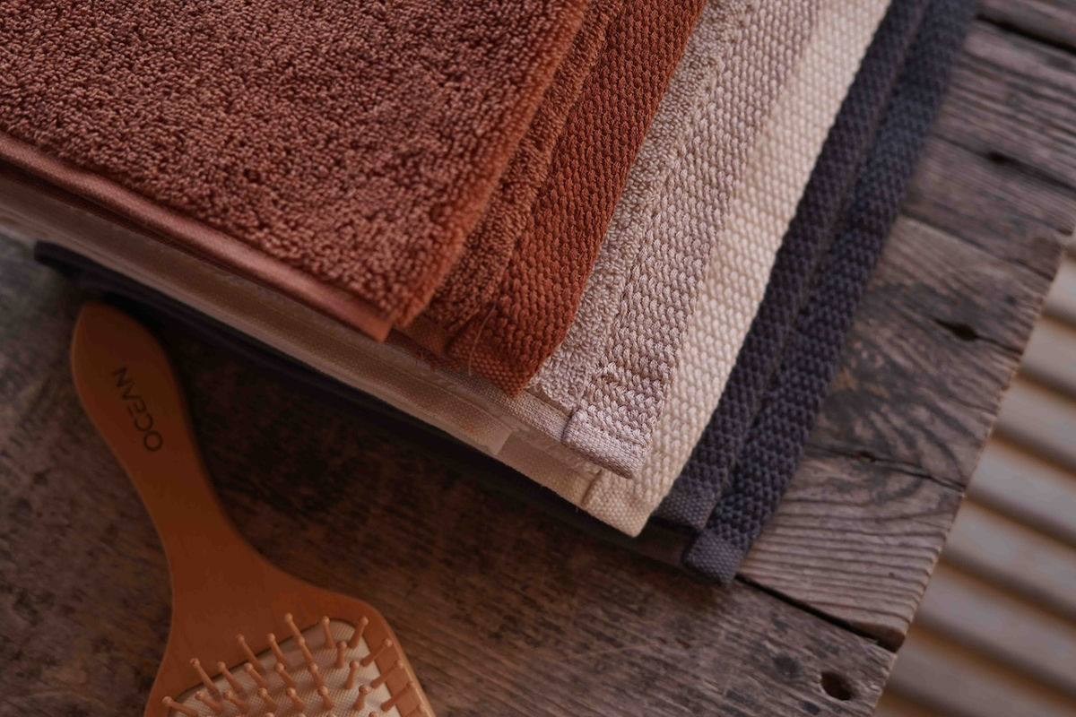 Stack of brown, beige, and gray towels on a wooden surface with a hairbrush.