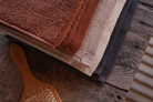 Stack of brown, beige, and gray towels on a wooden surface with a hairbrush.