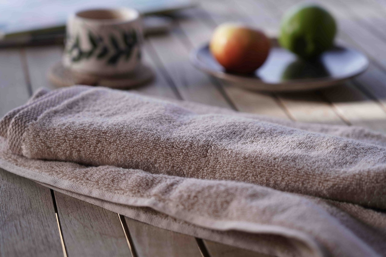 Brown towel on a wooden surface with a blurred background of a cup and fruits.
