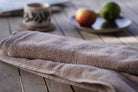 Brown towel on a wooden surface with a blurred background of a cup and fruits.