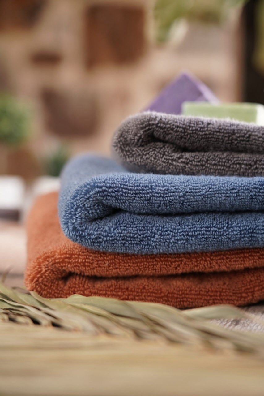 Stack of folded towels in orange, blue, and grey on a blurred natural background