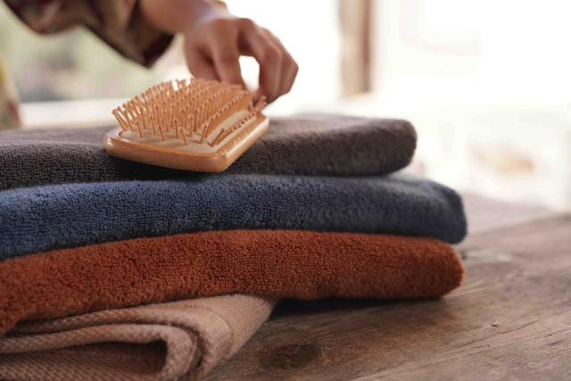 Stack of folded towels with a hairbrush on top, on a wooden surface.