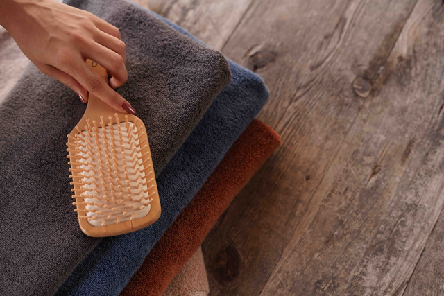 Hand holding a wooden brush over folded towels on a wooden surface