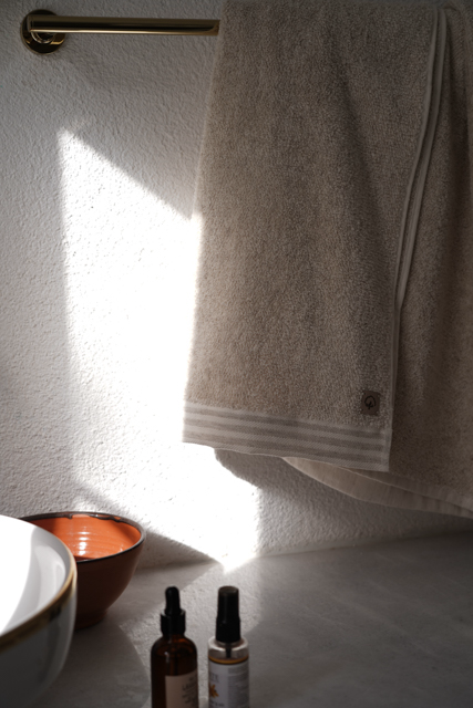 Beige towel hanging on a towel rack with a bowl and bottles on a surface below.