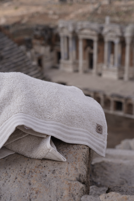 White towel with a logo on a stone surface, with ancient ruins in the background