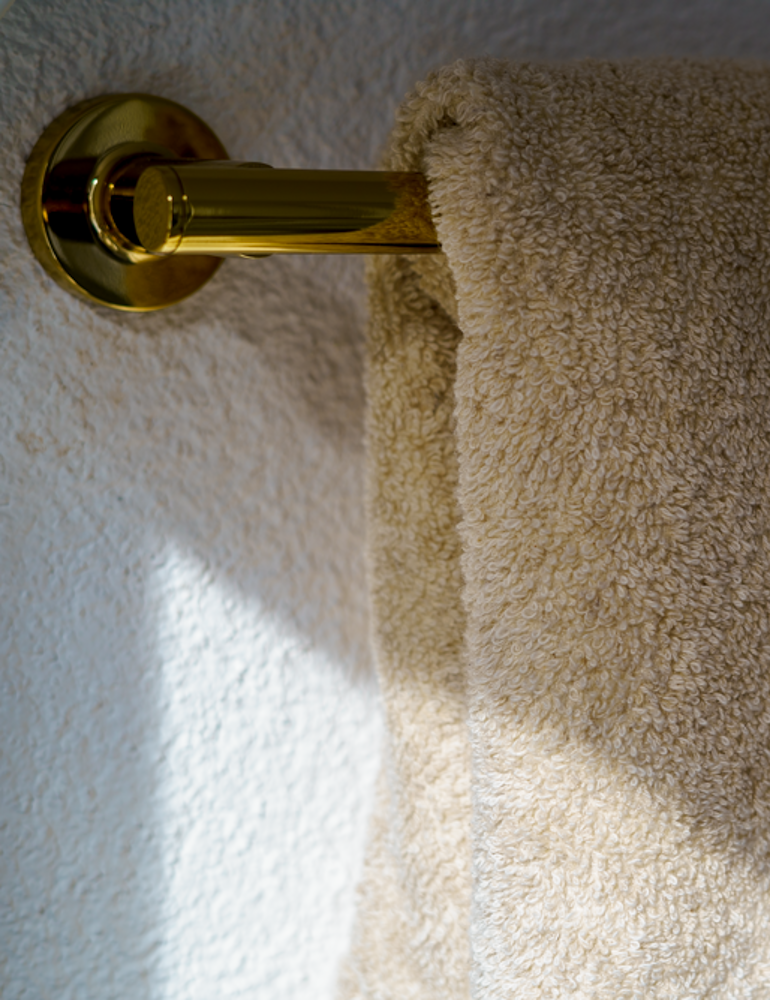 Beige towel hanging on a gold towel rack against a textured white wall