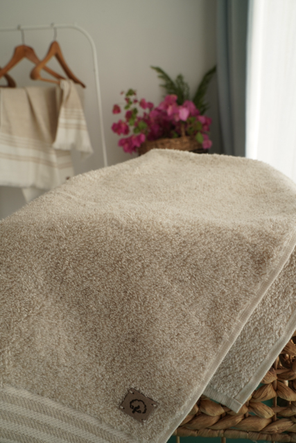 Close-up of a beige towel with a blurred background featuring a basket of flowers and hangers.