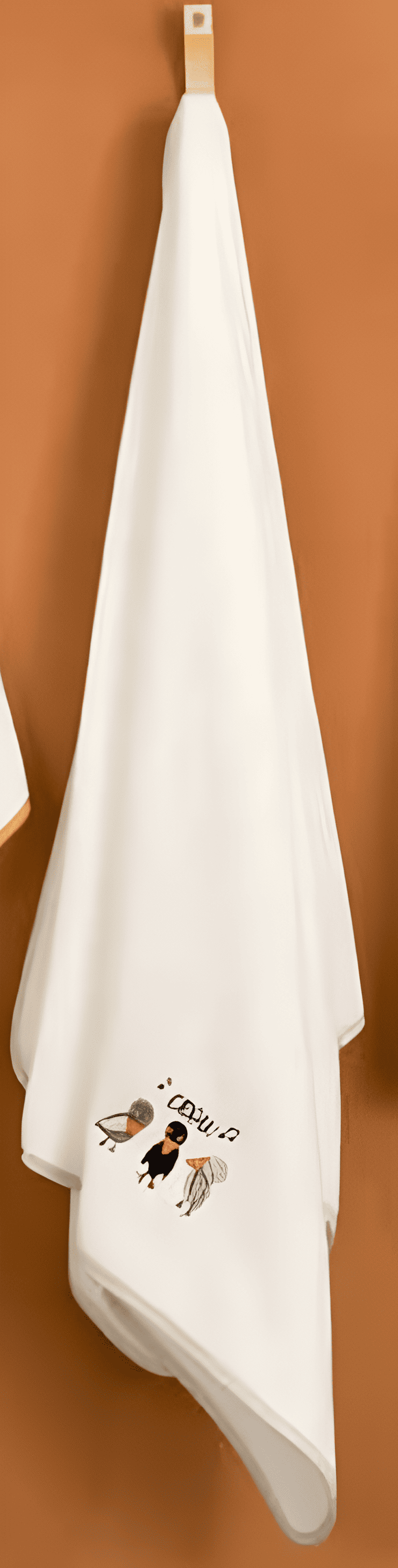 White towel with crow characters hanging on a wooden hook against a brown background