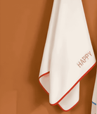 White towel with red border and 'HAPPY' text on a brown background