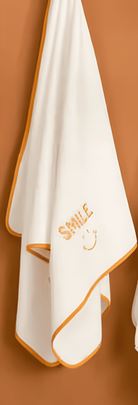 White towel with orange border and 'SMILE' text on a brown background